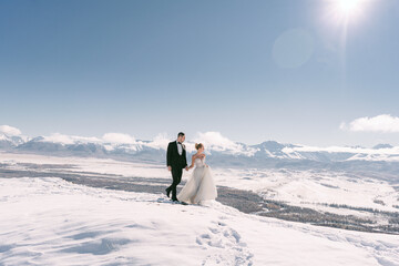 Bride and groom in a dress on a snowy road among the mountains in autumn in Altai