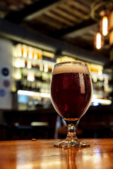 Tasty. Full glass of dark stout beer with drops on the side, wooden table in warm light of bar. Alcohol, entertainment, traditional drinks, Oktoberfest atmosphere concept. Modern bar, vertical crop.