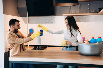 Pretty couple having fun and pretending fight with cleaning tools in kitchen.