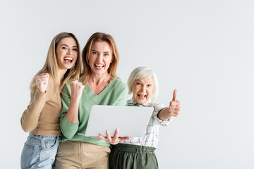 Obraz premium three generation of happy women looking at camera, showing thumb up and holding laptop isolated on white