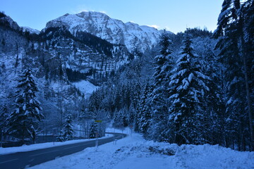 Road leading through winter landscape with trees and steep mountain covered with snow and ice