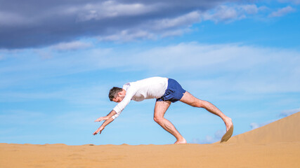 Fototapeta na wymiar Young athletic man doing acrobatics in the sand of the dunes in Gran Canaria