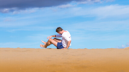 Naklejka na ściany i meble Young man falling and laughing on the sand in dunes in Gran Canaria