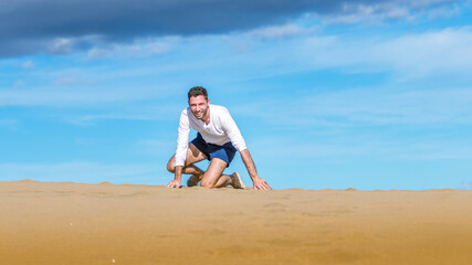 Fototapeta na wymiar Young man falling and laughing on the sand in dunes in Gran Canaria