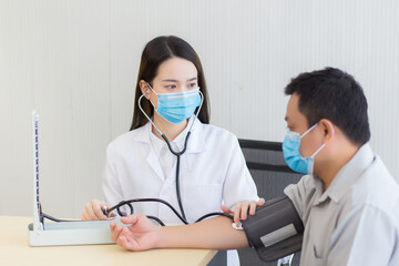 Young Asian woman doctor and a man patient wear medical face mask while check up his health in hospital to protect respiratory system from Corona virus 2019 (COVID-19) outbreak.