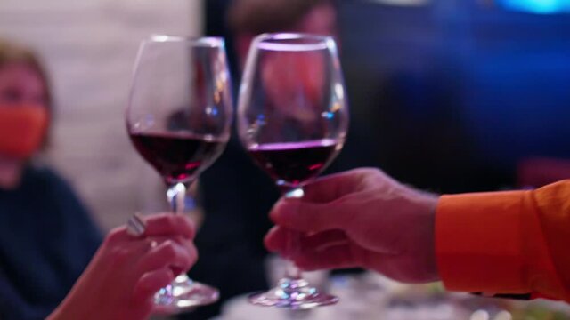 Close up and soft focused view of twa wine glasses half filled with wine in hands of man and woman. Defocused view of background.