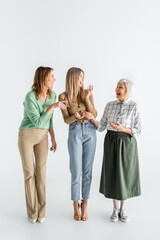 full length of three generation of happy women laughing while standing on white