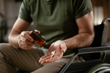 Sad unhappy depressed man in wheelchair is holding a pill in a hand. Close up of man holding handful of pills..