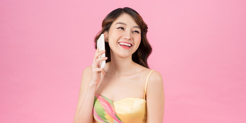 Portrait of a cute happy girl in dress talking on mobile phone and laughing isolated over pink background