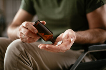 Sad unhappy depressed man in wheelchair is holding a pill in a hand. Close up of man holding handful of pills..