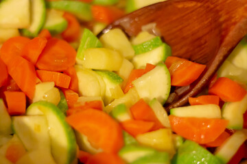 Close up of pre-cooked vegetables with a wooden service spoon. Cooking process.