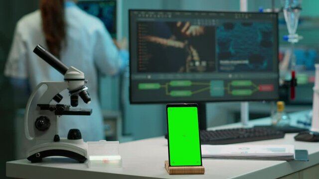 Display phone with green screen, mock up on template placed on desk in scientific lab while team of medical researcher scientists analysing virus evolution at digital monitor conducting experiment