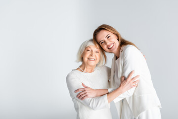 senior mother hugging with happy daughter isolated on grey