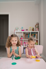 Naklejka premium Little girls with lovely faces play with clay molding shapes, learning through playing with colored plasticine developing creativity