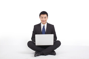 Portrait of young businessman sitting on ground with his laptop 