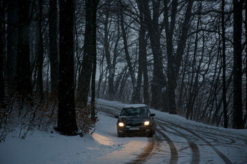 car on the road in the forest in a snowstorm