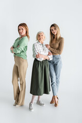 full length of three generation of women looking at camera and posing on white