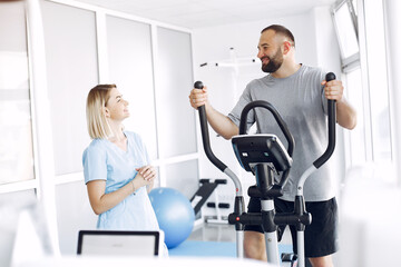 Fototapeta na wymiar A woman is a physiotherapist. A man is using a spin bike. The patient is having a treatment.