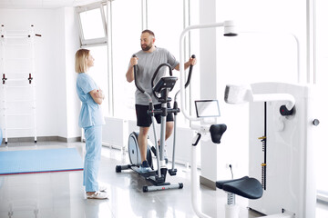 A woman is a physiotherapist. A man is using a spin bike. The patient is having a treatment.