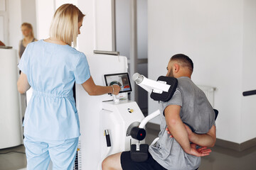 Patient has a rehabilitation in physiotherapy clinic. A therapist helps him. People are in the gym.