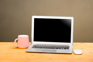 Mockup blank laptop screen with coffee on wooden table in coworking space.