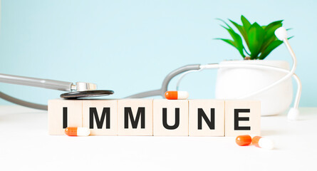 The word IMMUNE is written on wooden cubes near a stethoscope on a wooden background. Medical concept