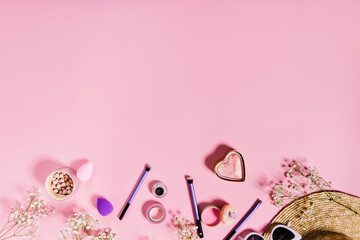 Blush, lilac makeup brushes and straw hat are located on isolated pink background