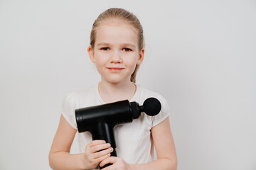 kid girl holds massage gun. medical-sports device helps to reduce muscle pain after training, helps to relieve fatigue, affects problem areas of body, improves condition of skin.