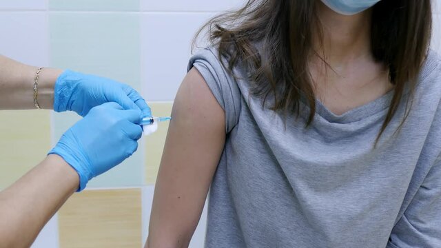 The doctor uses a hypodermic needle and syringe to inject medication as treatment. A nurse in protective gloves and a protective mask gives a vaccine injection to a patient in a clinic.