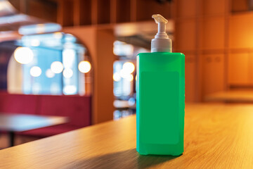 An unlabeled green bottle with a dispenser stands on a table in a restaurant. The background is blurred by photographic technique.
