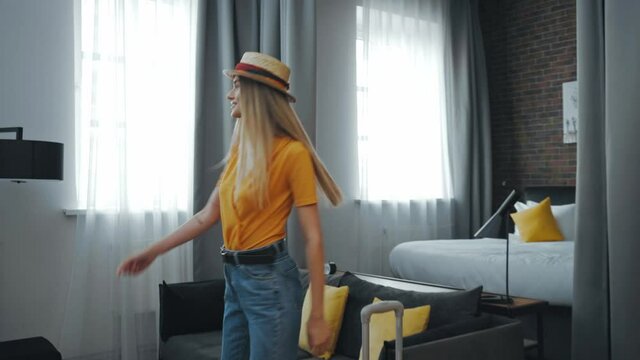 woman in straw hat walking with luggage in hotel room