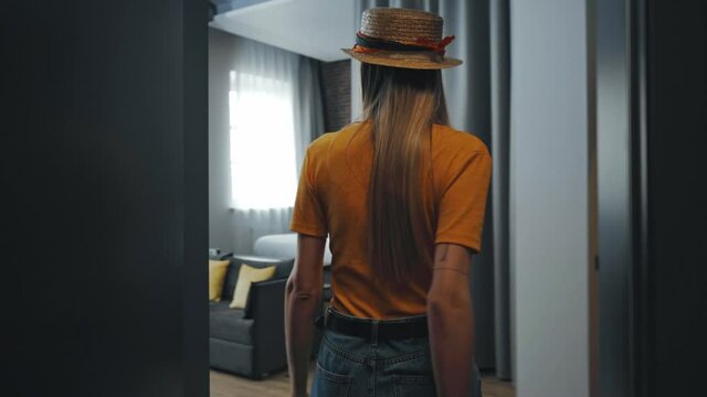 young woman in straw hat walking with luggage in hotel room