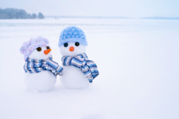 Two little cute snowmen in hats and scarves on the snow on a winter day, close-up. Holiday card with snowmen