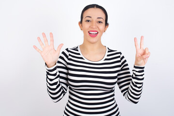 Young beautiful woman wearing stripped t-shirt against white background showing and pointing up with fingers number seven while smiling confident and happy.