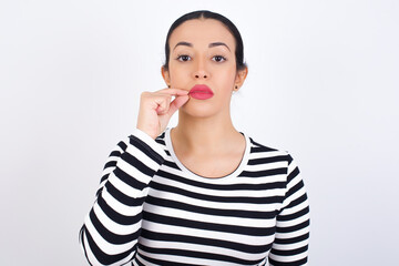 Young beautiful woman wearing stripped t-shirt against white background mouth and lips shut as zip with fingers. Secret and silent, taboo talking.