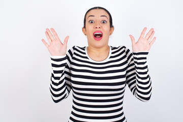 Naklejka premium Optimistic Young beautiful woman wearing stripped t-shirt against white background raises palms from joy, happy to receive awesome present from someone, shouts loudly, Excited model screaming.