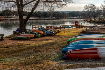 Canoes lined up on the shore of a lake with a dock and a campground in the background, Inks Lake,...