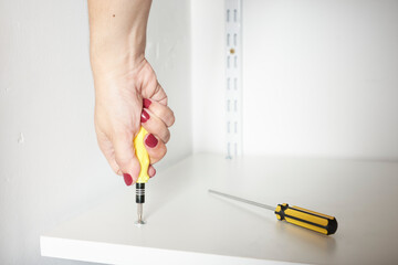 Hand of a young woman tightening a screw with a screwdriver, securing a shelf