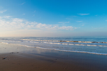 relaxing and gentle calming waves flowing into a beach at sundown, with a vivid blue sky and reflection. calming fresh air walks into nature during corona virus lockdowns