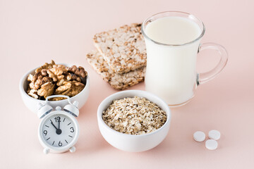 Good sleep. Foods for good sleep - milk, walnuts, crispbread, oatmeal, sleping pill and alarm clock on pink background