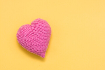 Handmade for Valentine's Day. Knitted big pink heart on a yellow background. Copy space