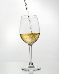 Vertical image.Pouring white wine into the glass against white background