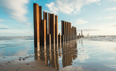 Large rusty steel construction pillars in the sand on a sunny beach, with blue sky and calm waves. The steel girders are rusty. Building and construction on the coast. Development and building © dannyburn