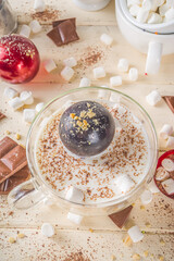 Hot chocolate bomb, with marshmallow and chocolates and nuts,  Woman's hand dropping chocolate bomb into cup with milk.