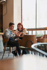 A couple of teenagers having fun while watching something, using their phones, sitting in a cafe together on a daytime