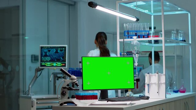 Team of scientists working in background of modern laboratory using computer with green screen, mockup display, chroma key monitor, analysing experiment evolution, high tech development lab.