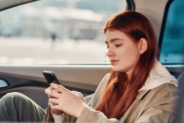 Portrait of teenage girl looking focused at the screen while using her phone, sitting in the car