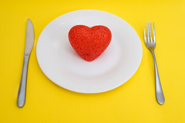 Fototapeta na wymiar Red heart on a white plate and cutlery on a yellow background