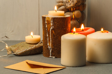 Fototapeta na wymiar Burning thick white candles in wooden and stone candlesticks and a craft envelope on the table. close-up