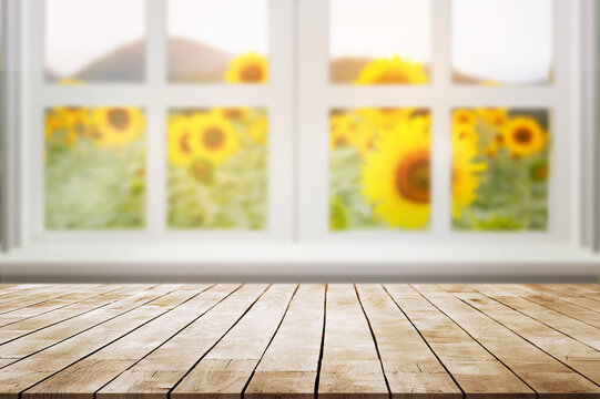 Empty wooden desk with white window against blured beautiful sunflower field with sunlight